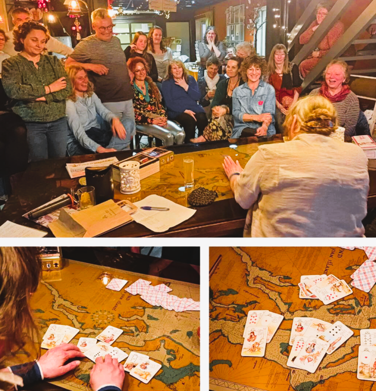 Een vrouw zit aan een grote tafel, omringd door geïnteresseerde deelnemers. Ze legt kaarten uit in een live demonstratie. 